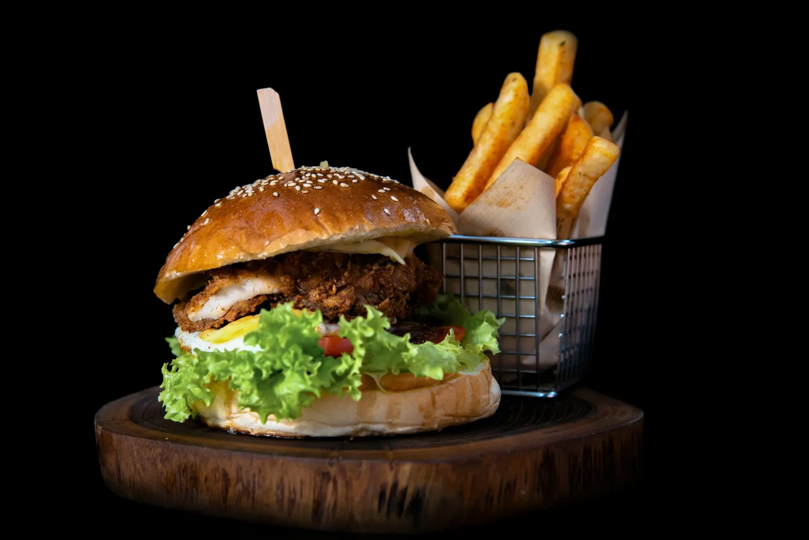 Un burger garni de salade, à côté d’un panier de frites, sur une planche en bois